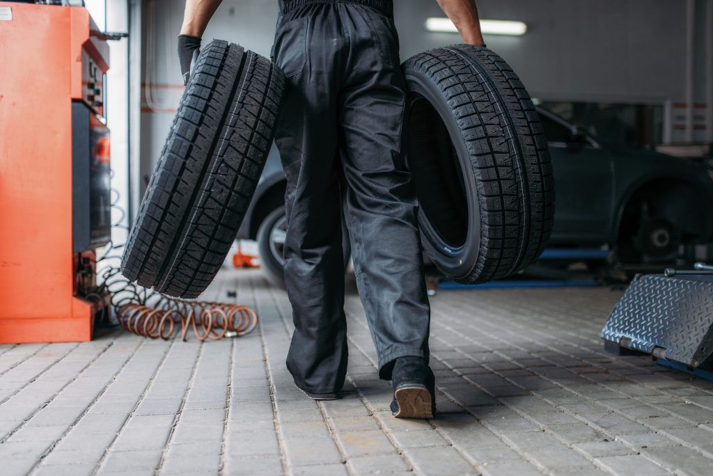 Auto mechanic holds two tires, repairing service